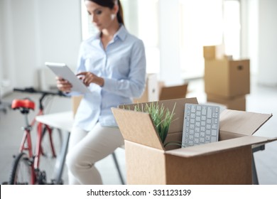 Business Woman Moving In A New Office, She Is Using A Digital Tablet, Selective Focus, Open Cardboard Box On Foreground