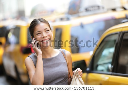 Business woman on smart phone in New York City, Manhattan walking in dress suit holding doggy bag smiling and laughing, Young multiracial Asian Caucasian professional female businesswoman in her 20s.