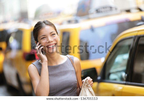Business woman on smart phone in New York City,\
Manhattan walking in dress suit holding doggy bag smiling and\
laughing, Young multiracial Asian Caucasian professional female\
businesswoman in her\
20s.