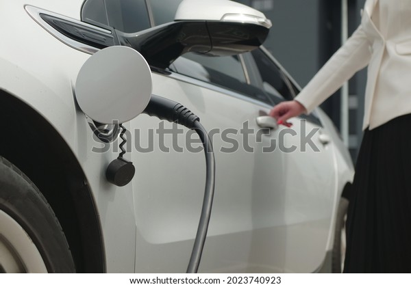 Business\
woman opens or closes the door of an electric car. Eco friendly\
alternative energy green environment\
concept