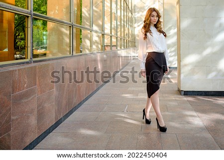 Business Woman outfit for office. Fashionable woman wears high-heels shoes, braun asymmetric skirt and a creme blouse, on a building background. [[stock_photo]] © 