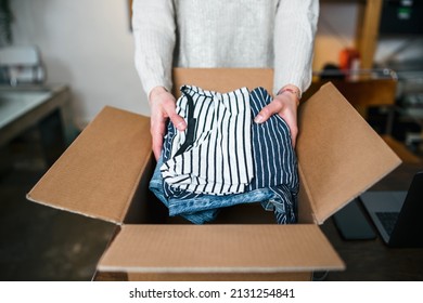 Business woman prepares a package in a cardboard box for shipping with clothes from her online store - Millennial sells second-hand used dresses in her home - Start up concept - Shutterstock ID 2131254841
