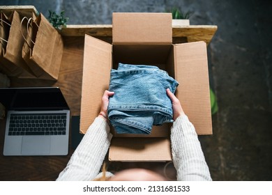 Business Woman prepares a package in a cardboard box for shipping with clothes from her online store - Millennial sells second-hand used clothing in her home - Start up concept