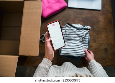 Business Woman prepares a parcel for shipping in a cardboard box with clothes from her online store - Millennial sells second-hand used clothing in her home using the smartphone application - Start up