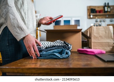 Business woman prepares a parcel for shipping in a cardboard box with clothes from her online store - Millennial sells second-hand used dresses in her home using the smartphone application - Start up