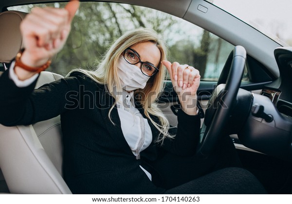 Business woman in protection mask sitting\
inside a car using\
antiseptic