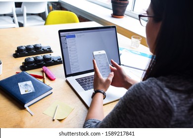 Business Woman Reading Text Message On Mobile Phone During Work On Pc Laptop Computer, Sitting At Wooden Table In Office Interior. Female Bookkeeper Online Booking On Cellphone 