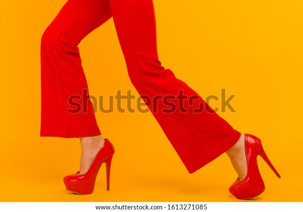 The business woman running somewhere hurrying up\
isolated on yelow background. Stylish red heels and pants on thin\
female legs