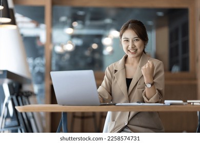 A business woman or secretary working on a laptop expresses her joy while looking at the laptop screen. Asian female employees express the excitement of success and bonuses. - Shutterstock ID 2258574731