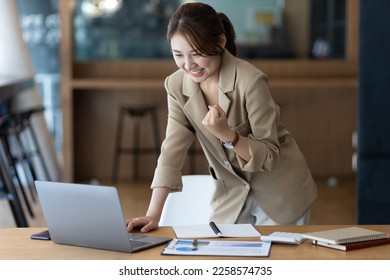 A business woman or secretary working on a laptop expresses her joy while looking at the laptop screen. Asian female employees express the excitement of success and bonuses. - Shutterstock ID 2258574735