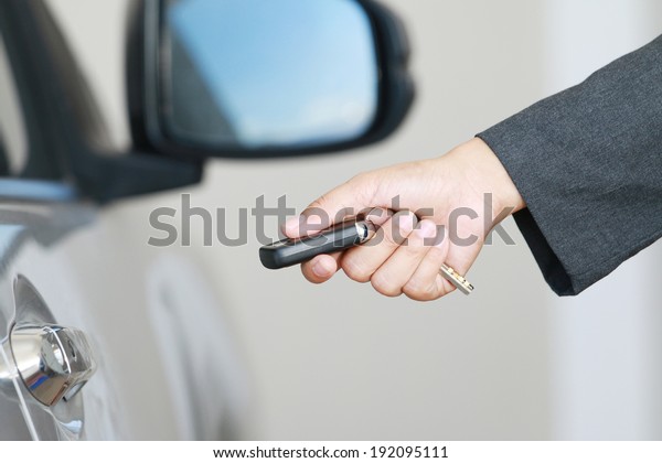 Business woman show a remote car key and\
operate. car\
background.