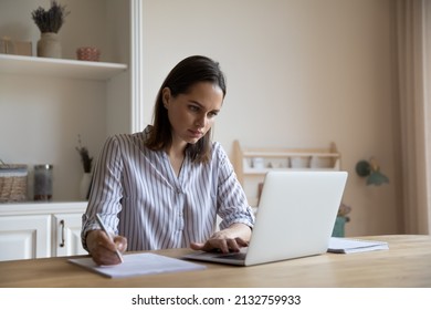 Business woman sit at table holds pen make correction in document, check written data, do paperwork looks at laptop, work from home in quarantine, student prepare essay, learn at home use tech concept - Shutterstock ID 2132759933