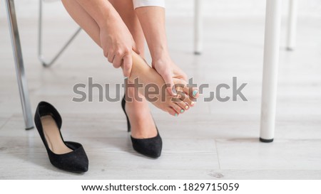 A business woman sits in an office on a chair, takes off her high-heeled shoes and massages her tired feet
