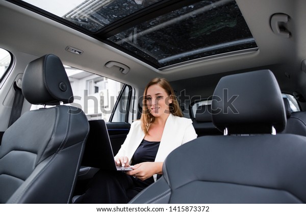 Business woman sitting in the back passenger seat\
working on laptop