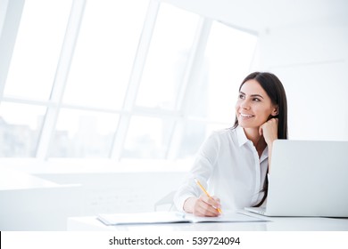 Business woman sitting by the table with laptop and looking away in office