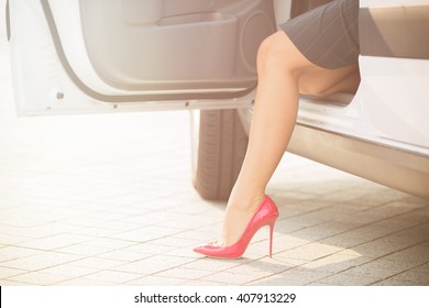 Business Woman Sitting In Her Car. She Is Going To Get Out From The Car. Slim And Slender Woman's Leg On High Heels Looking From The Car. Toned Image.