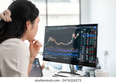 Business woman is sitting on her working desk in the office. She is stressed and disappointed at the stock trading market value as she is staring computer screen looking at charts and data analysis. - Powered by Shutterstock