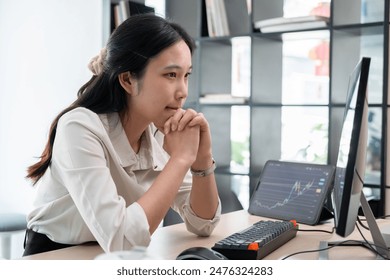 Business woman is sitting on her working desk in the office. She is stressed and disappointed at the stock trading market value as she is staring computer screen looking at charts and data analysis. - Powered by Shutterstock