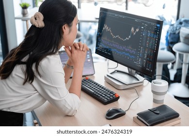 Business woman is sitting on her working desk in the office. She is stressed and disappointed at the stock trading market value as she is staring computer screen looking at charts and data analysis. - Powered by Shutterstock