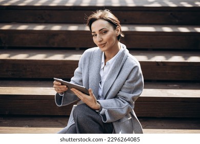 Business woman sitting on stairs and working on tablet - Powered by Shutterstock