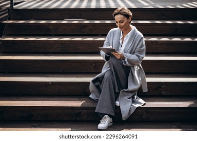 Business woman sitting on stairs and working on tablet - Powered by Shutterstock