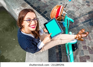 Business woman sitting with tablet on the fo?ntain in the city with bicycle on background