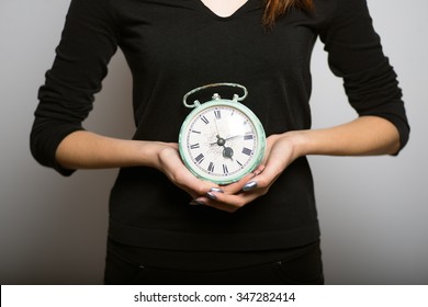Business woman slender shows a  alarm clock, studio shot isolated on the gray background