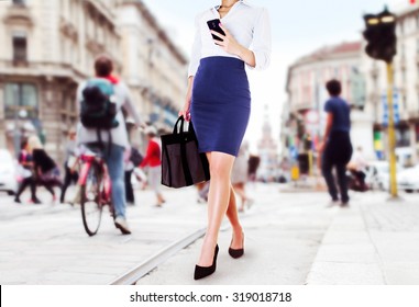 A business woman with smart phone walking in the street. Beautiful legs with office fashion. bag and dhoes in the city. 