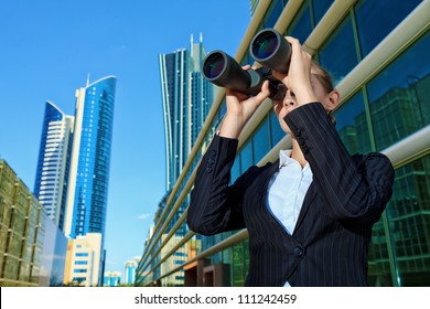 Business woman standing in the big city and purposefully looking through the binoculars.
