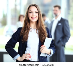 Business Woman Standing In Foreground With A Tablet In Her Hands, Her Co-workers Discussing Business Matters In The Background