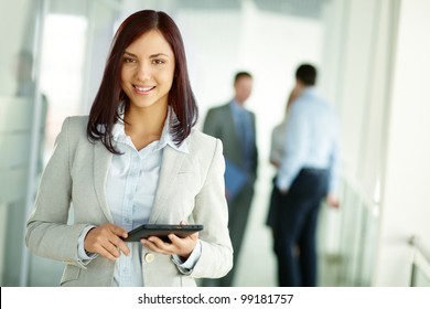 Business Woman Standing In Foreground With A Tablet In Her Hands, Her Co-workers Discussing Business Matters In The Background, Tilt Up