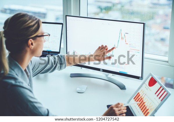 Business woman study financial market to\
calculate possible risks and profits.Female economist accounting\
money with statistics graphs pointing on screen of computer at\
desktop. Quotations on\
exchange