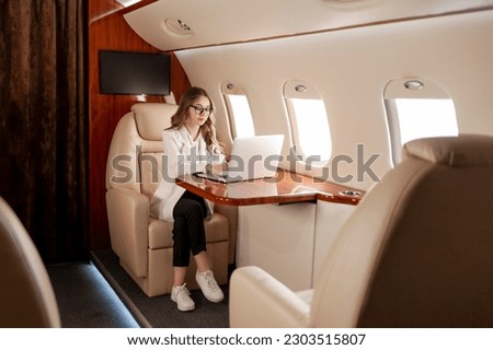 business woman in suit and glasses flies in private luxury jet and works on laptop, girl manager financier uses computer and types in plane Foto stock © 