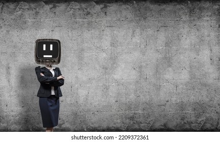 Business Woman In Suit With Old TV Instead Of Head Keeping Arms Crossed While Standing Inside Empty Room With Gray Dark Wall On Background.