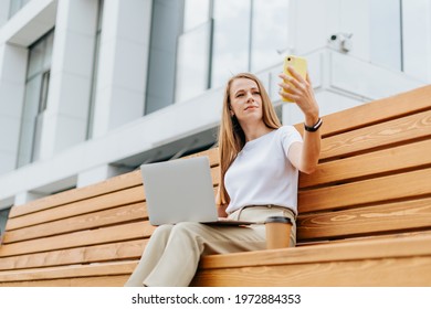 Business Woman In Suit Taking A Selfie On Cellphone And Working At Laptop Sit Down On Bench Outside. Happy Student Lady Girl Having A Video Chat With Phone, Distance Learning And Online Education.