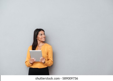 Business Woman In Suit Which Holding Tablet Computer And Looking Away. Isolated Gray Background