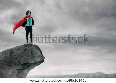 Business woman as a super hero on the peak of a mountain