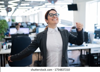 Business Woman Takes Off The Mask In The Office At The End Of Quarantine. Coronavirus Over Time To Return To Work. The Girl Breathes Freely And Smiles. Victory Over The Pandemic. Return To Normal.