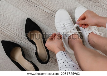 Business woman takes off white leather sneakers and puts on black high heel shoes. The girl changes shoes before work