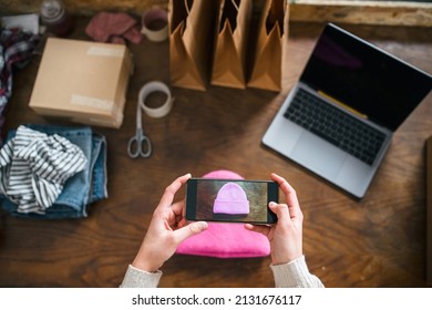 Business woman takes a photo with her smartphone of the hat she wants to sell  before putting the advert online - Millennial uses websites to market second-hand clothing don't use - Start up concept - Shutterstock ID 2131676117