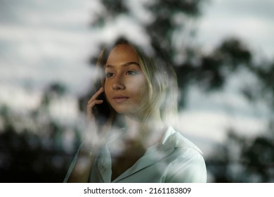 Business Woman Talking On The Phone In An Office Behind The Window With Outdoor Reflection In The Glass