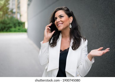 Business Woman Talking On Smartphone In Front Of Corporate Building. Portrait Of Female Manager Talking On Cell Phone By Grey Wall