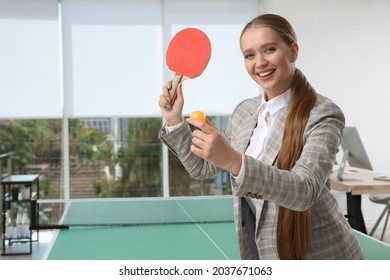 Business woman with tennis racket and ball near ping pong table in office. Space for text