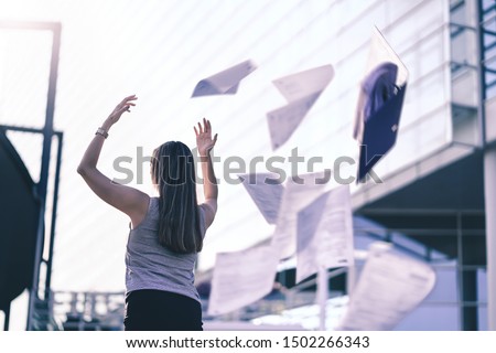 Business woman throwing work papers in the air. Stress from workload. Person going home or leaving for vacation. Employee got fired. Job or project done. Difficult workday over. Outside of office.