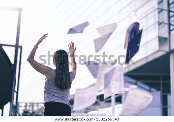 Business woman throwing work papers in the air.\
Stress from workload. Person going home or leaving for vacation.\
Employee got fired. Job or project done. Difficult workday over.\
Outside of office.