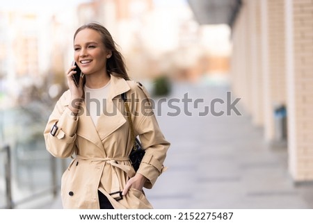 A business woman in trench coat talks on her mobile phone outdorrs