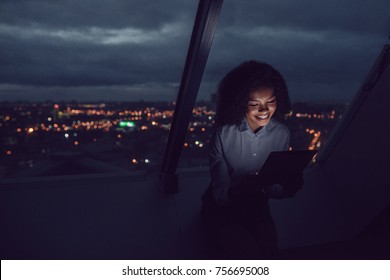 Business Woman Uses A Tablet Sitting By The Window In The Office On A Background Of A Night City.