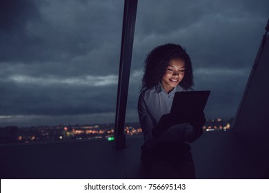 Business woman uses a tablet sitting by the window in the office on a background of a night city.