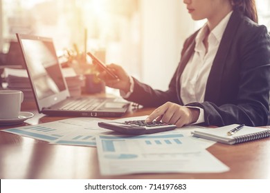 Business Woman Using Calculator And Writing Make Note With Calculate. Woman Working At Office With Laptop And Documents On His Desk