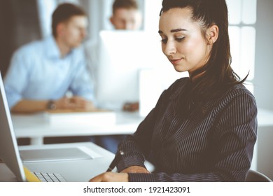 Business Woman Using Computer At Workplace In Modern Office. Brunette Secretary Or Female Lawyer Looking At The Camera And Happy Smiling. Working For Pleasure And Success